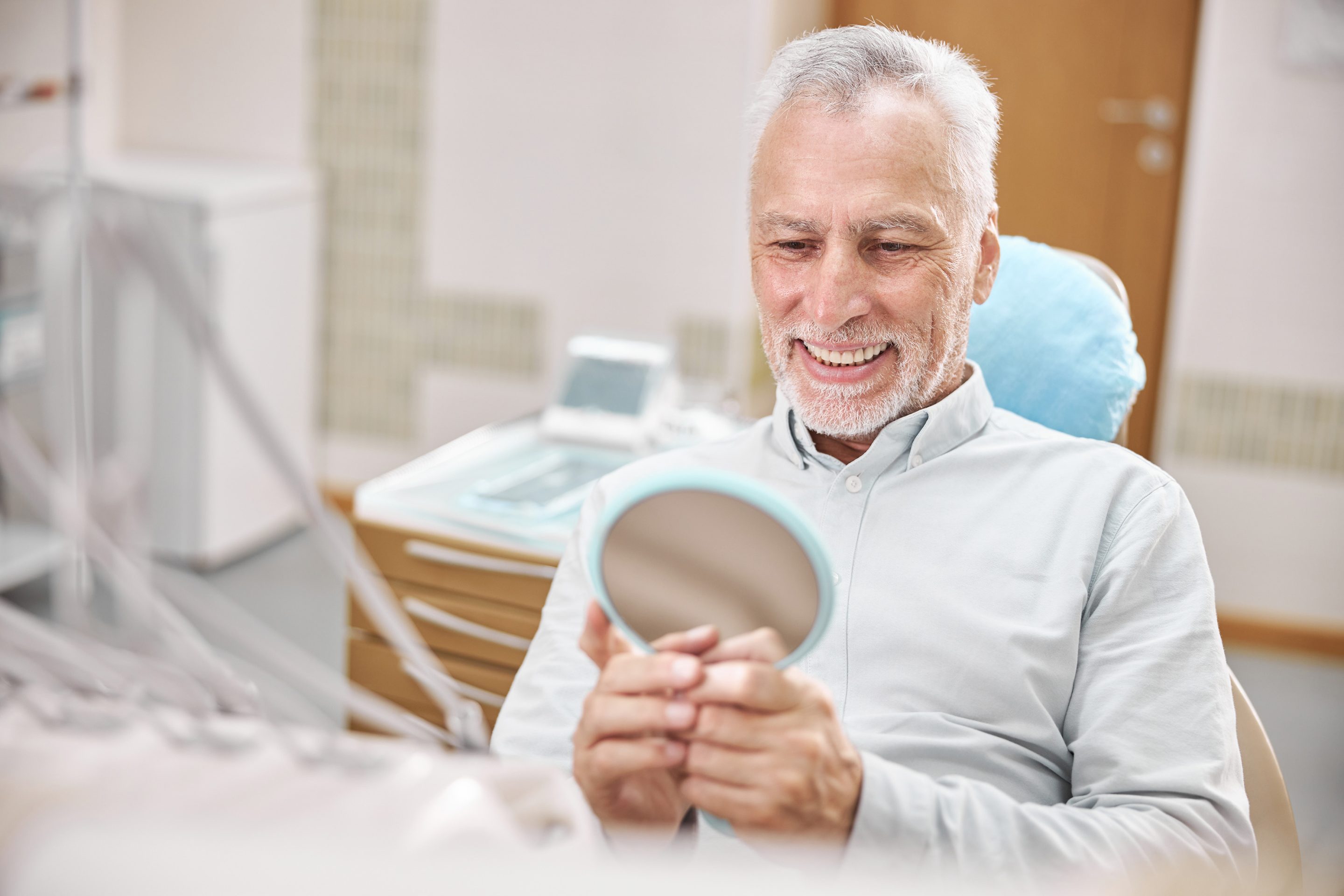 elderly man looking into mirror at dentist - Scholes Family Dental